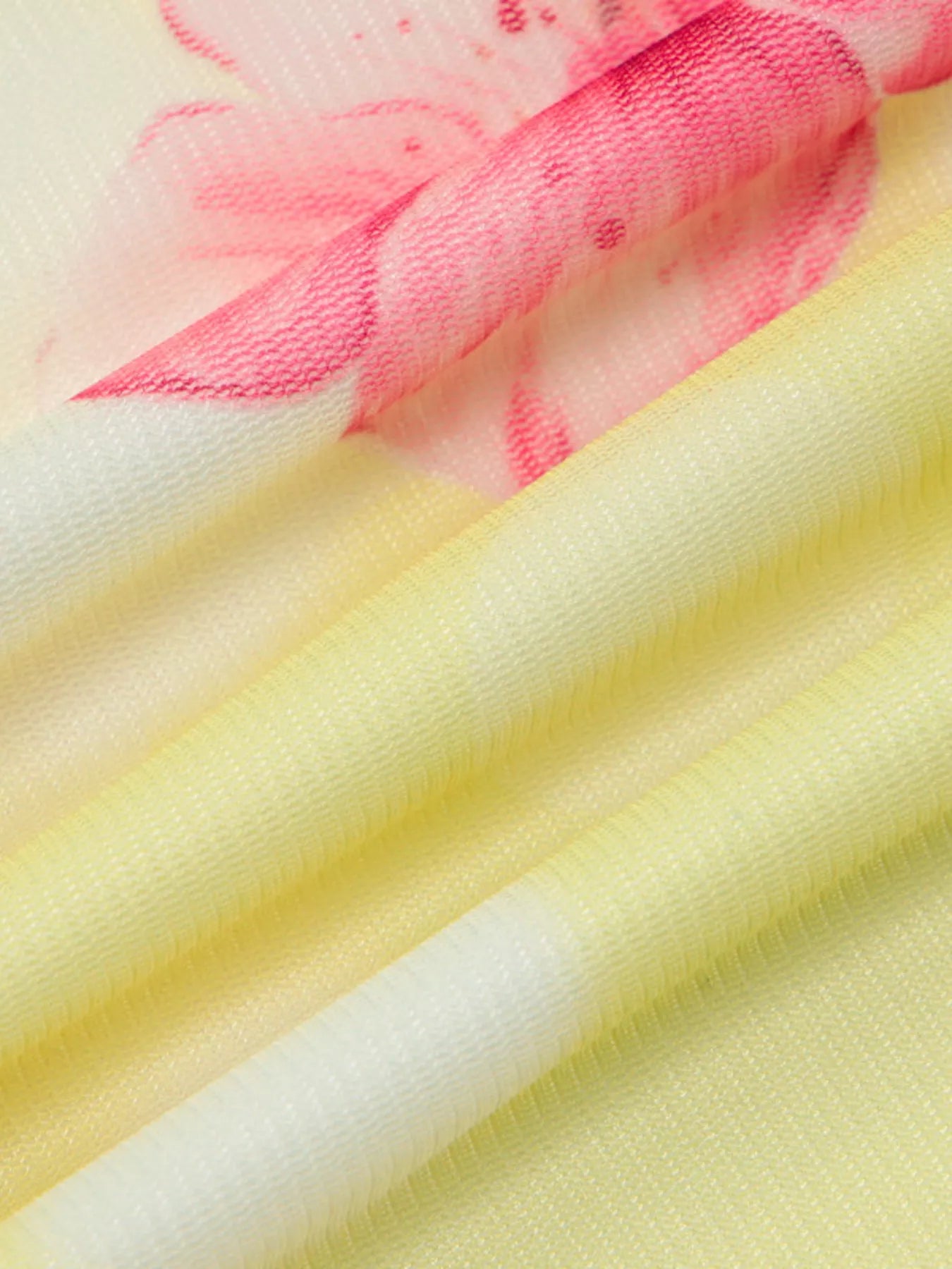 Close-up of yellow sheer fabric with pink floral print, draped in diagonal folds