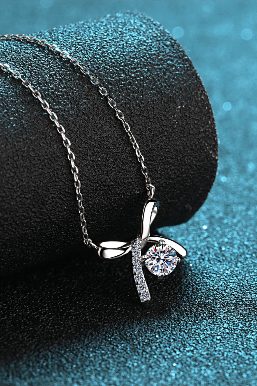 Moissanite sterling silver necklace with bow pendant and round center gemstone, side view