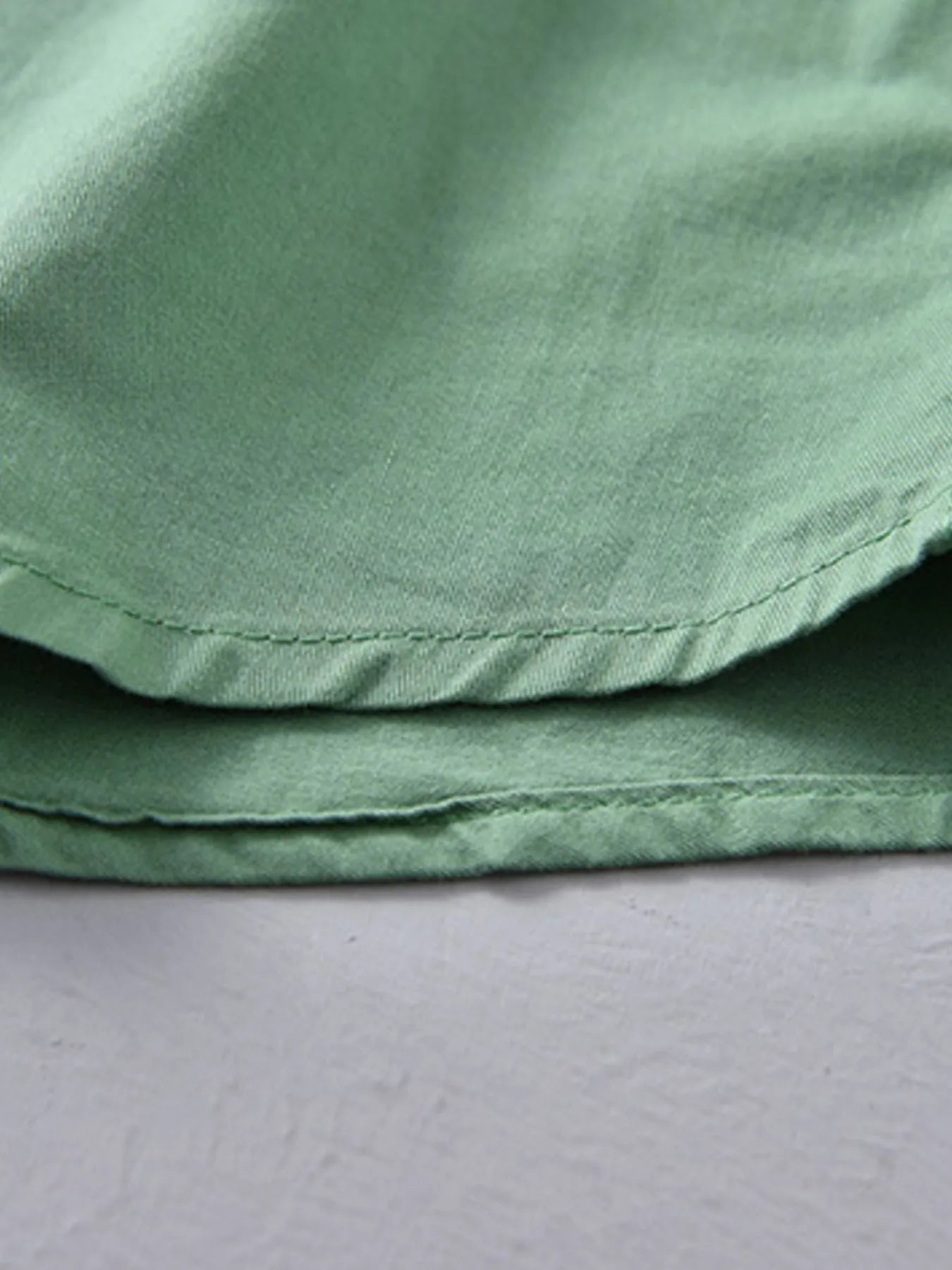 Green short-sleeve button-up shirt hem with stitched edge