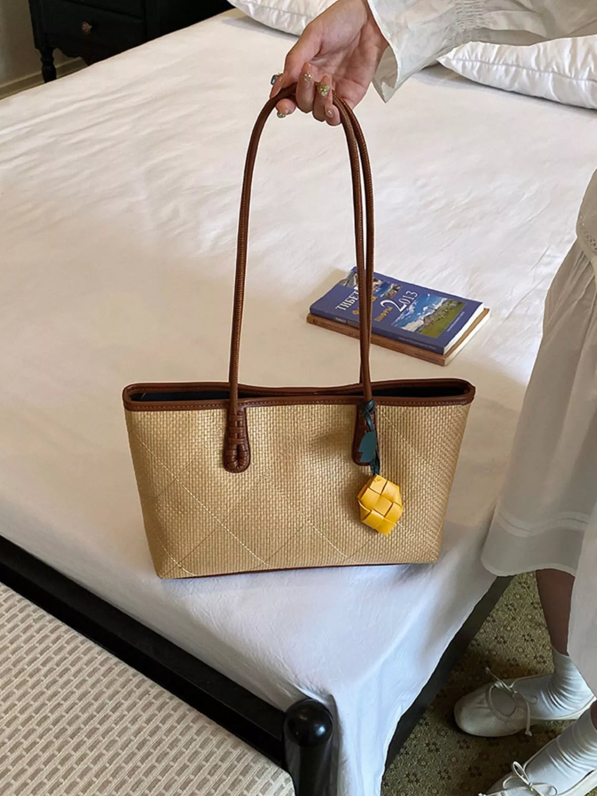 Beige leather tote-style shoulder bag with brown handles and yellow charm