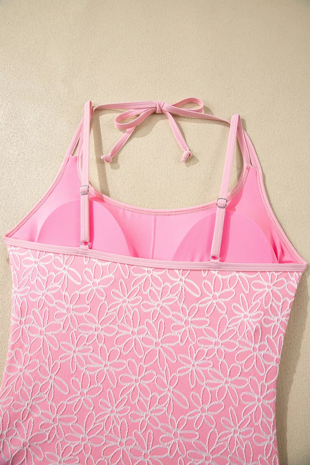 Blush pink floral halter one-piece swimsuit with tie-back detail, shown on hanger