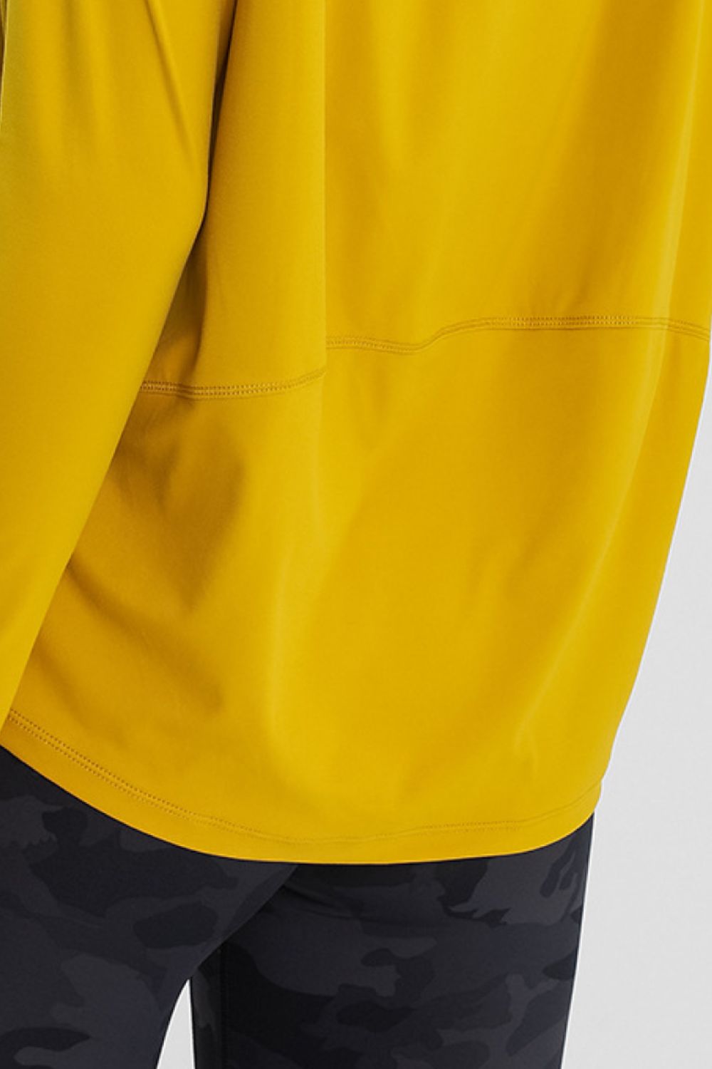 Loose-fit active top in mustard yellow, close-up of stitched hem and drape.