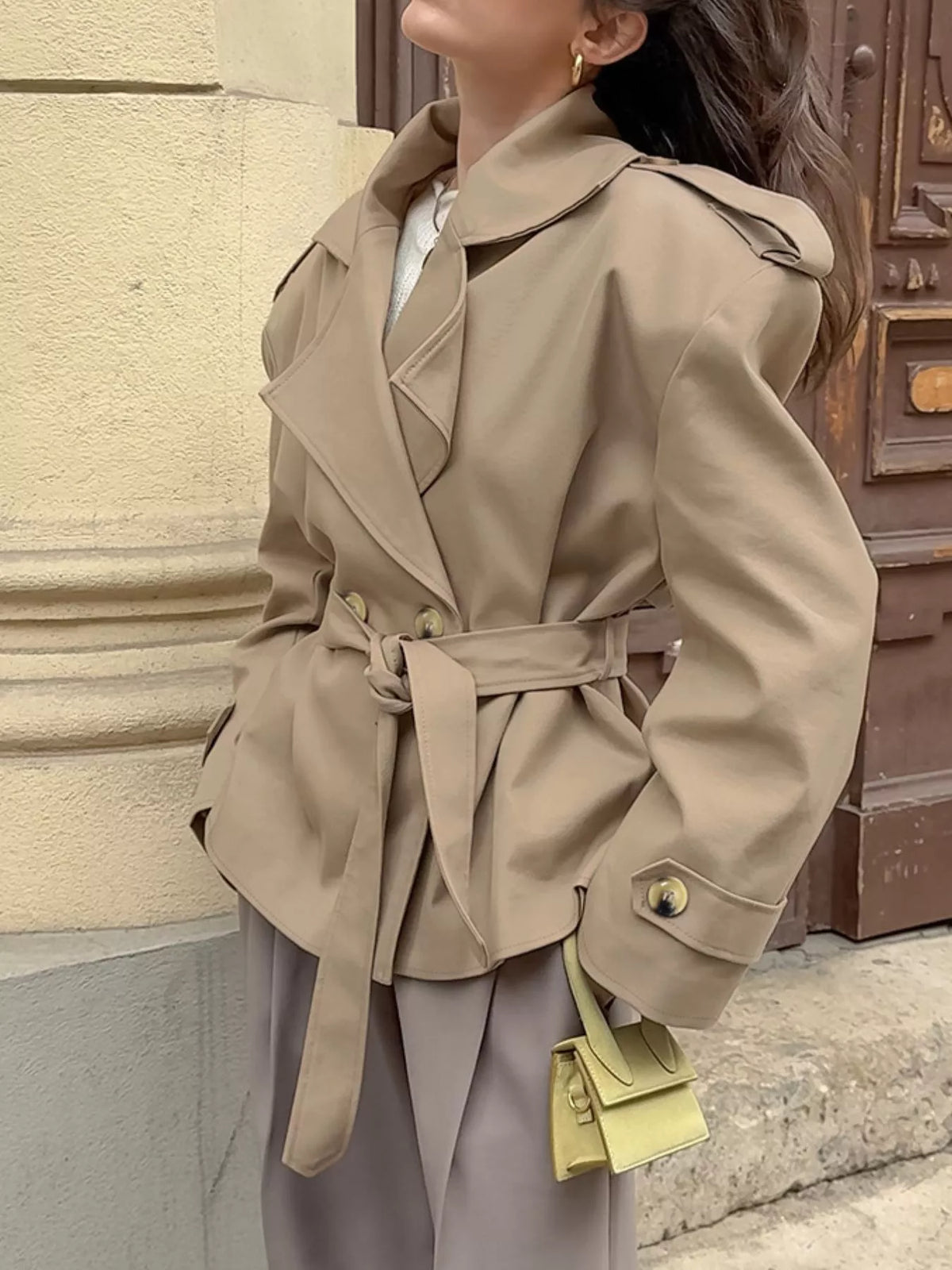 Khaki belted trench coat from the side with lapels and gold buttoned sleeve cuff