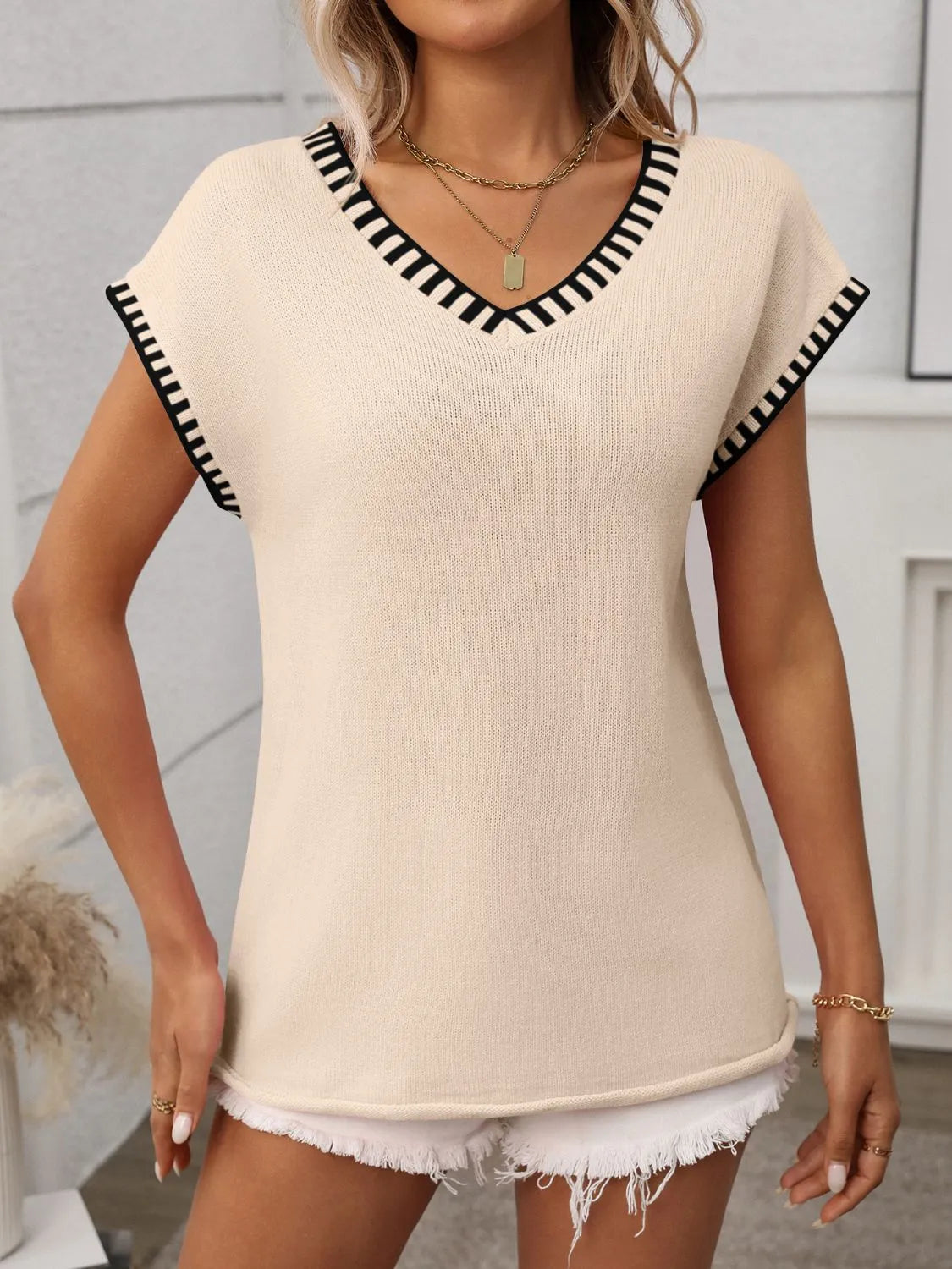 Tan knit V-neck top with black contrast trim, short sleeves, and straight hem