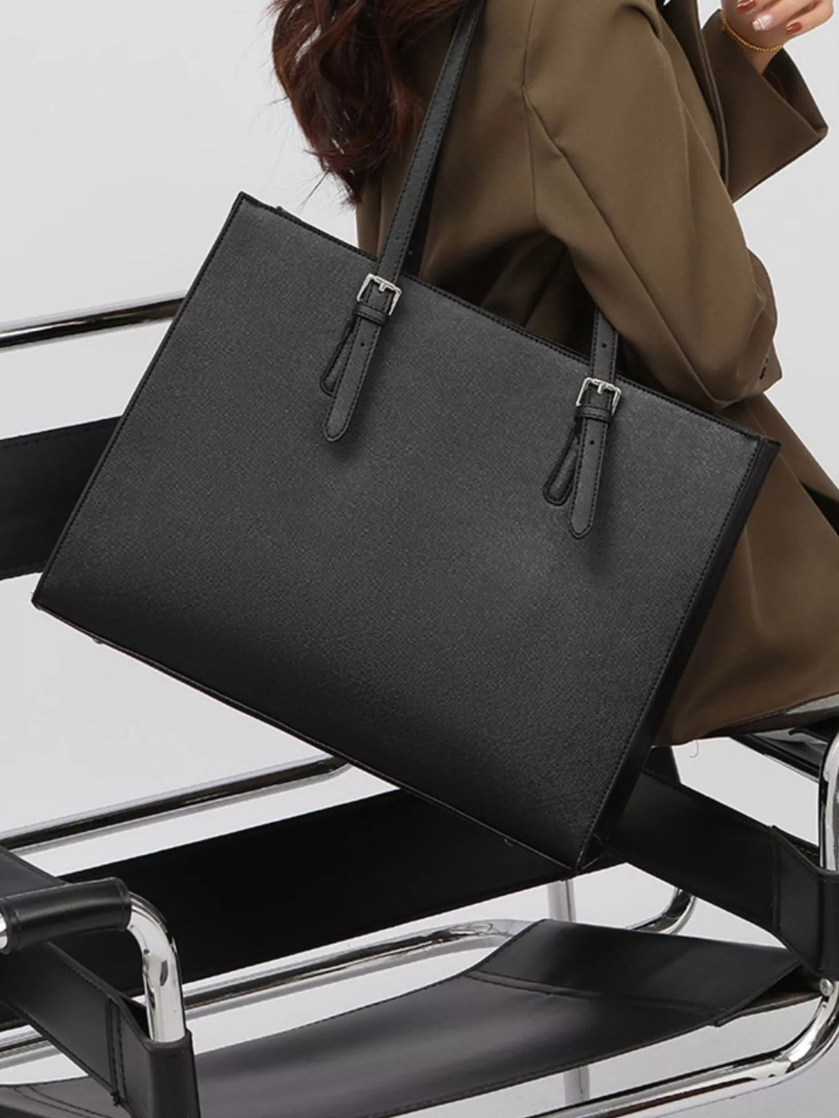 Black large tote bag showing front panel and two vertical strap buckles; wide base.