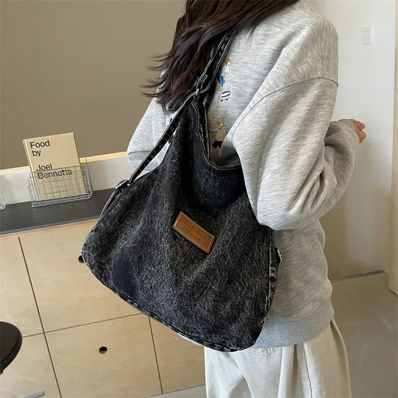 Dark denim shoulder bag with adjustable strap and rectangular leather logo patch