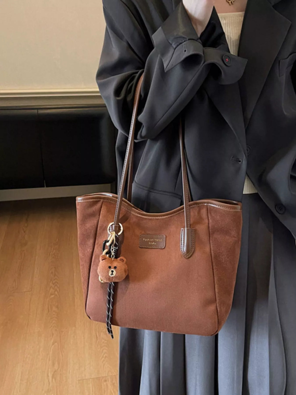 Brown suede tote bag with long handles, zipper top, and bear keychain charm