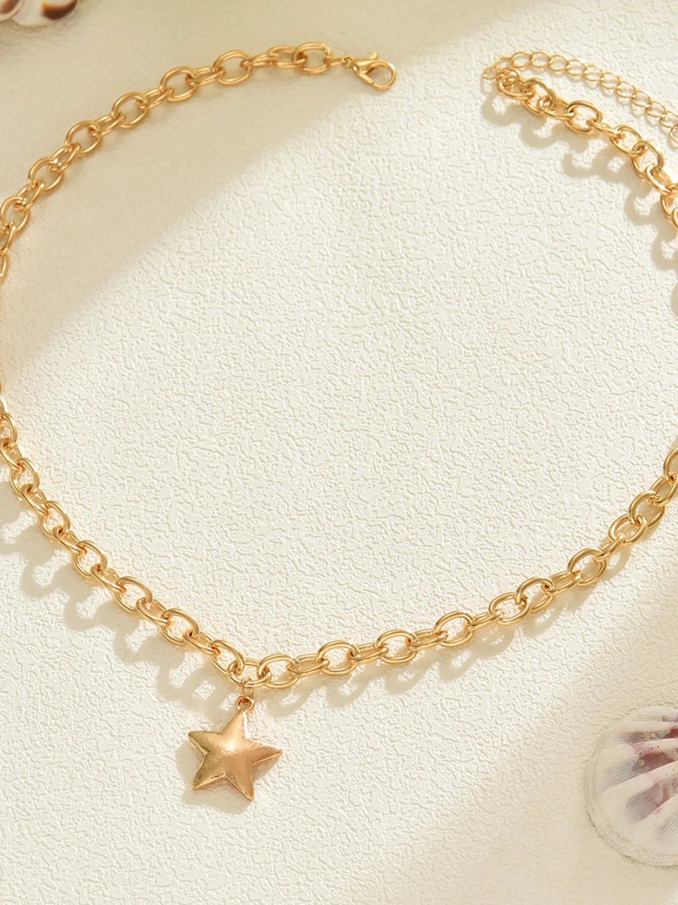 Gold star pendant chain necklace laid flat, oval link chain with small star charm