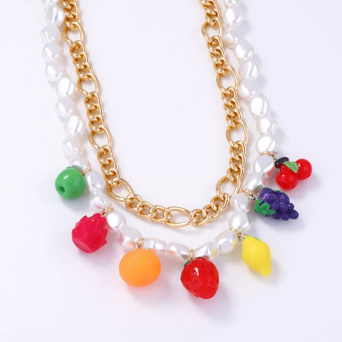 Double-layer charm necklace close-up with gold links, white pearls, and fruit charm cluster