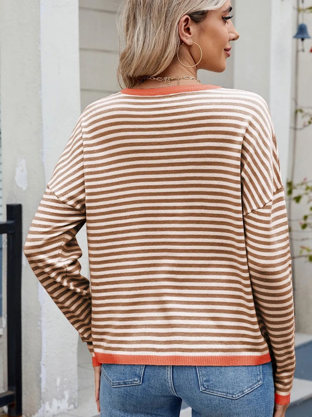 Back view of beige and white striped round-neck long-sleeve sweater with orange trim