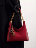 Wine red suede shoulder bag with gold chain strap and tassel charm.