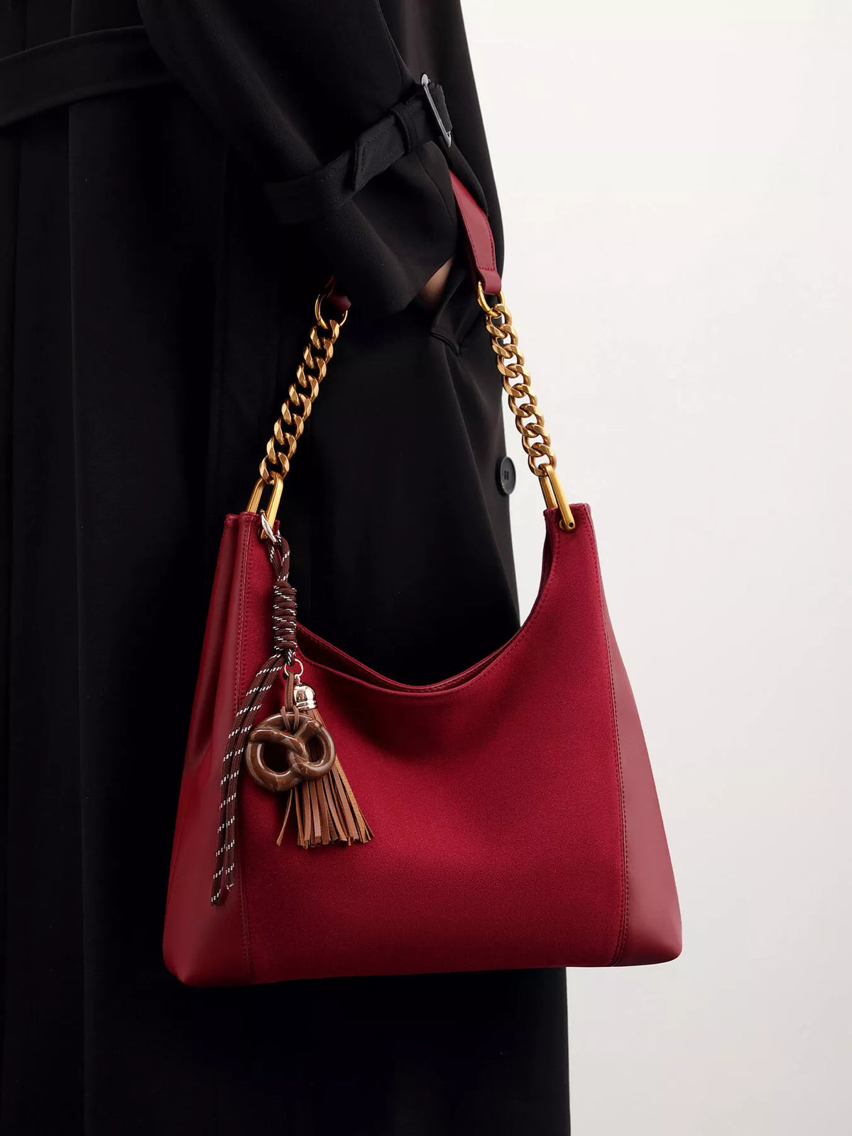 Wine red suede shoulder bag with gold chain strap and tassel charm.