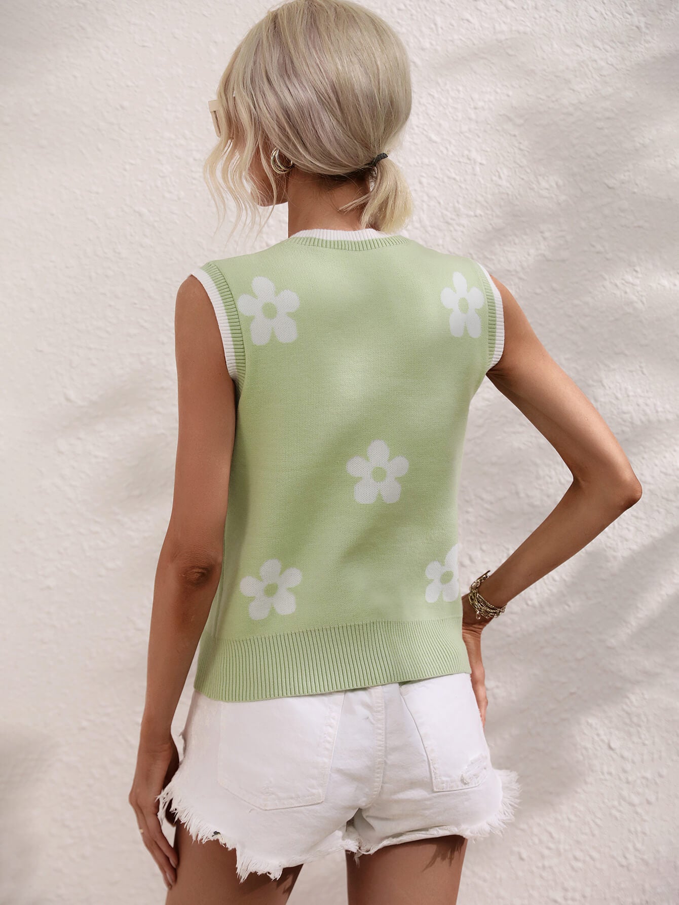 Light green sleeveless sweater vest, back view with white flower motifs and ribbed hem.