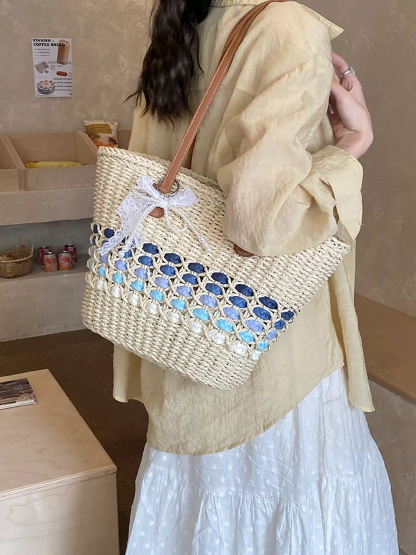 Woven straw shoulder bag with white bow accent and blue lattice panel, brown leather handles
