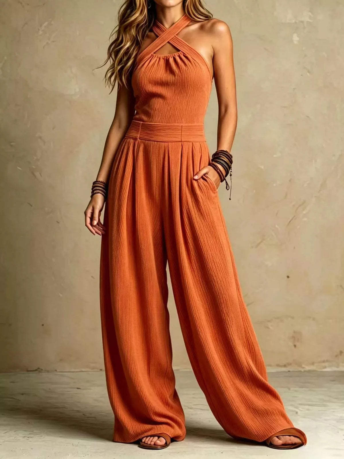 Orange halter wide-leg jumpsuit with crisscross neckline and gathered waist detail.