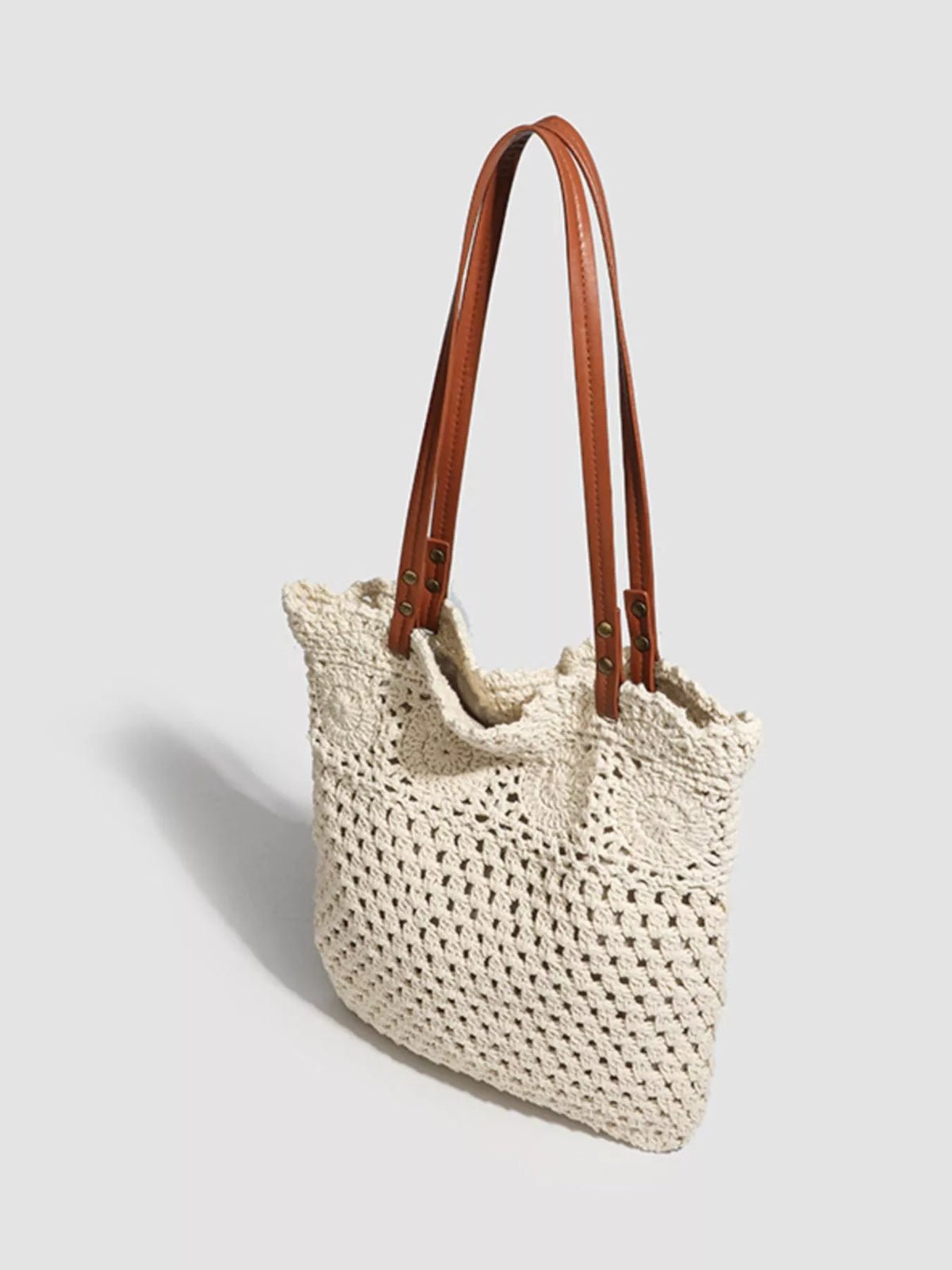 Crochet knit tote handbag with brown leather straps and structured rectangular base.