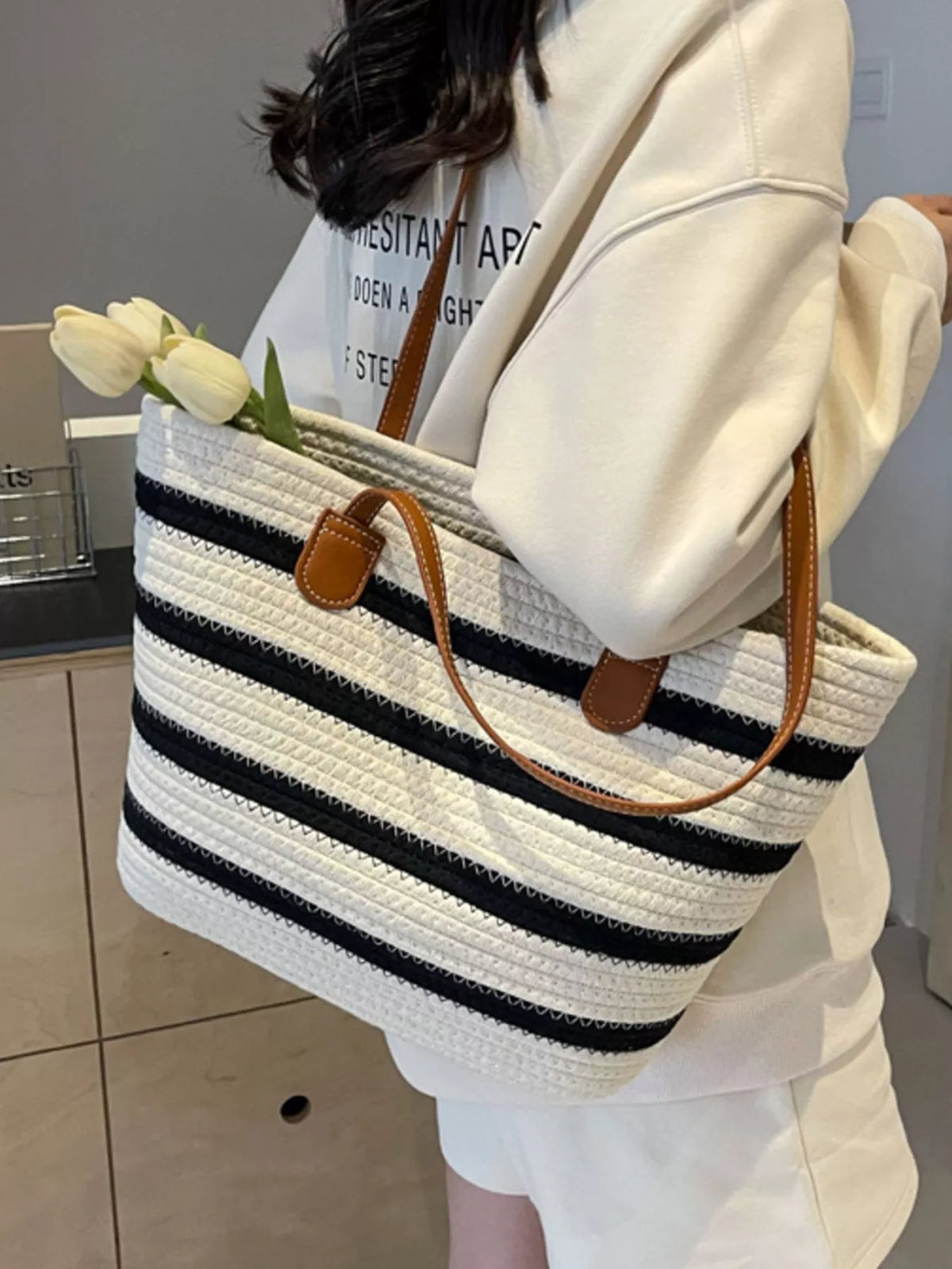 Striped straw tote bag with brown double handles, white body with navy horizontal stripes