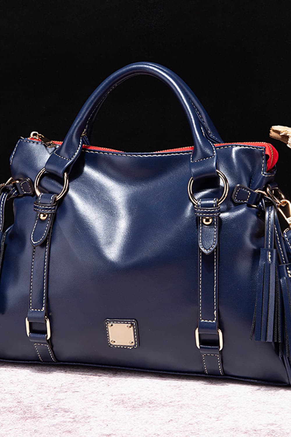PU leather handbag in dark blue with tassels, top handles, and front square patch.
