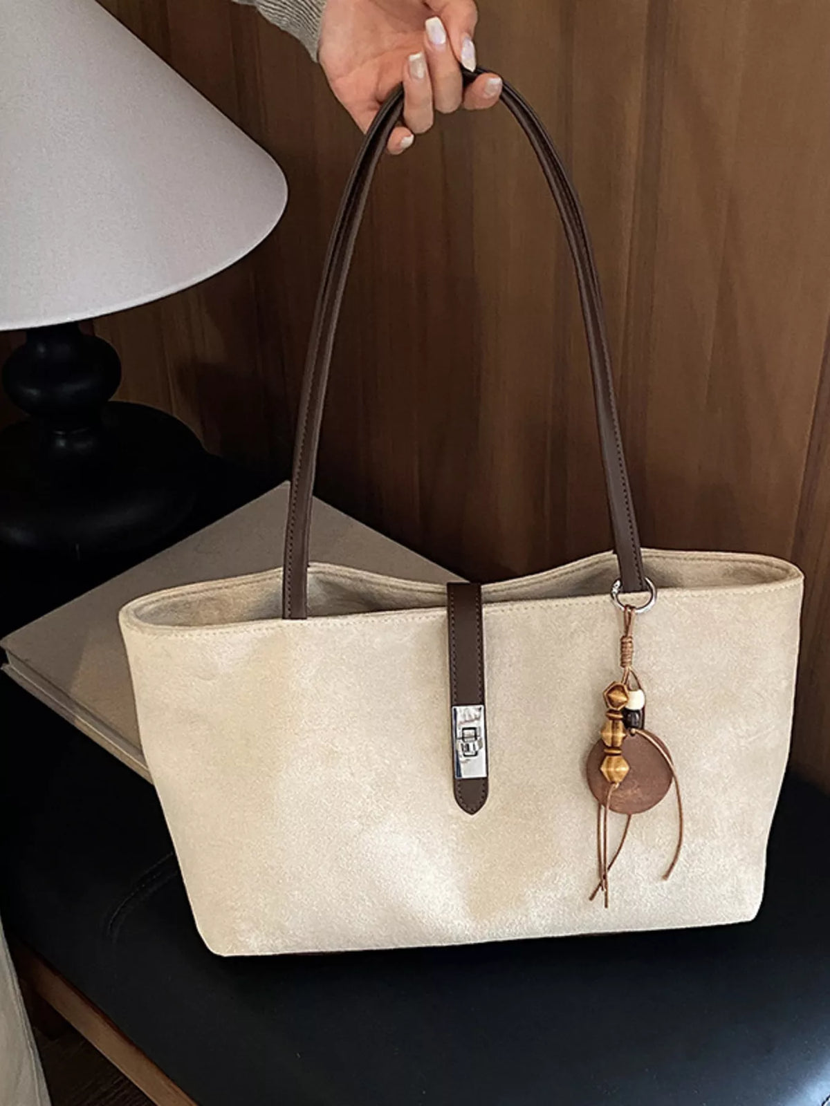 Beige suede tote bag close view, with top handles, buckle strap, and charm