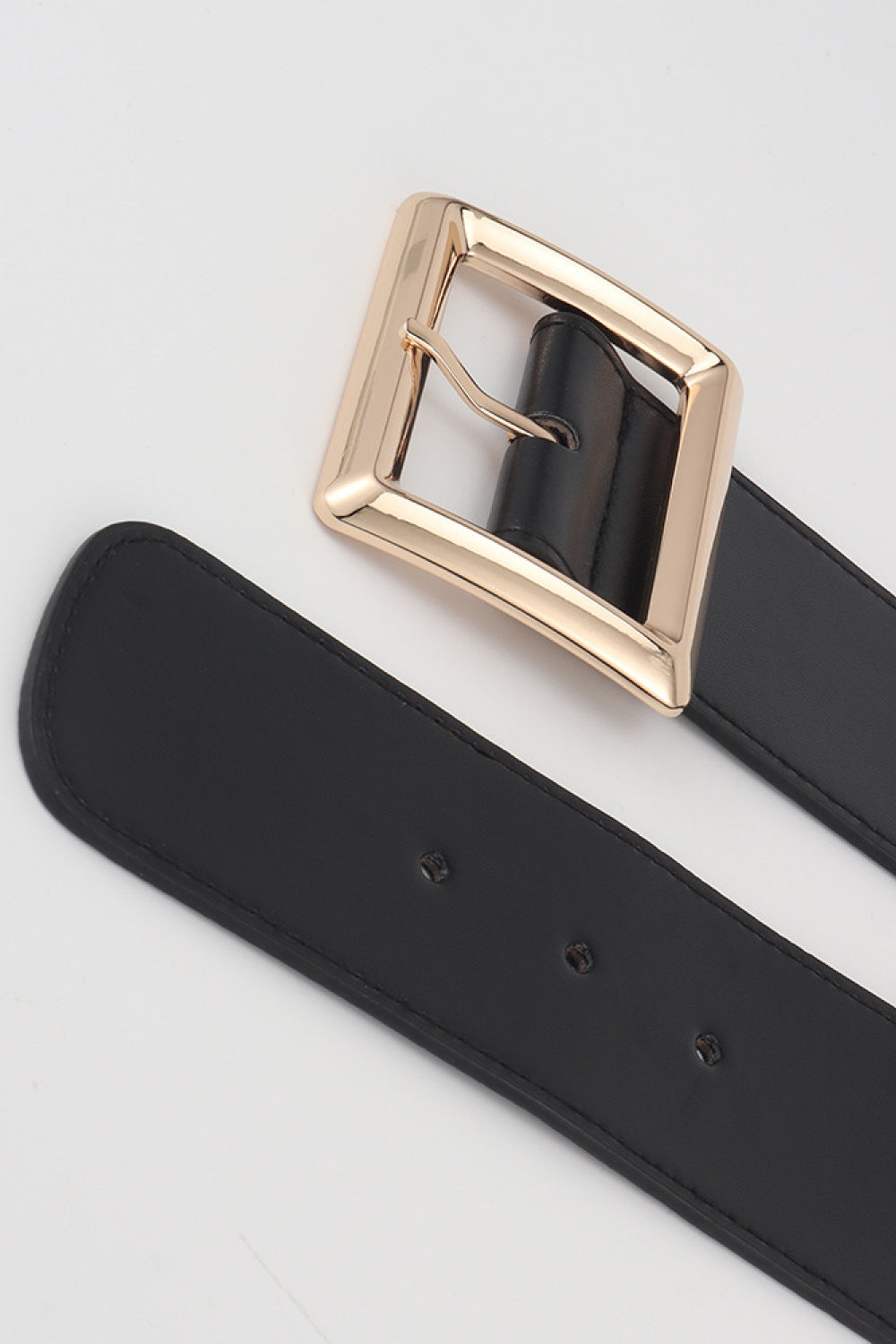 Black elastic belt close-up with rectangular gold buckle and adjustment holes.
