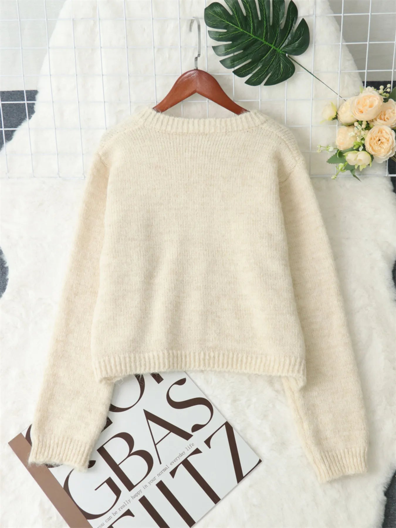 Cream cardigan sweater laid out, back view with ribbed hem and full sleeves