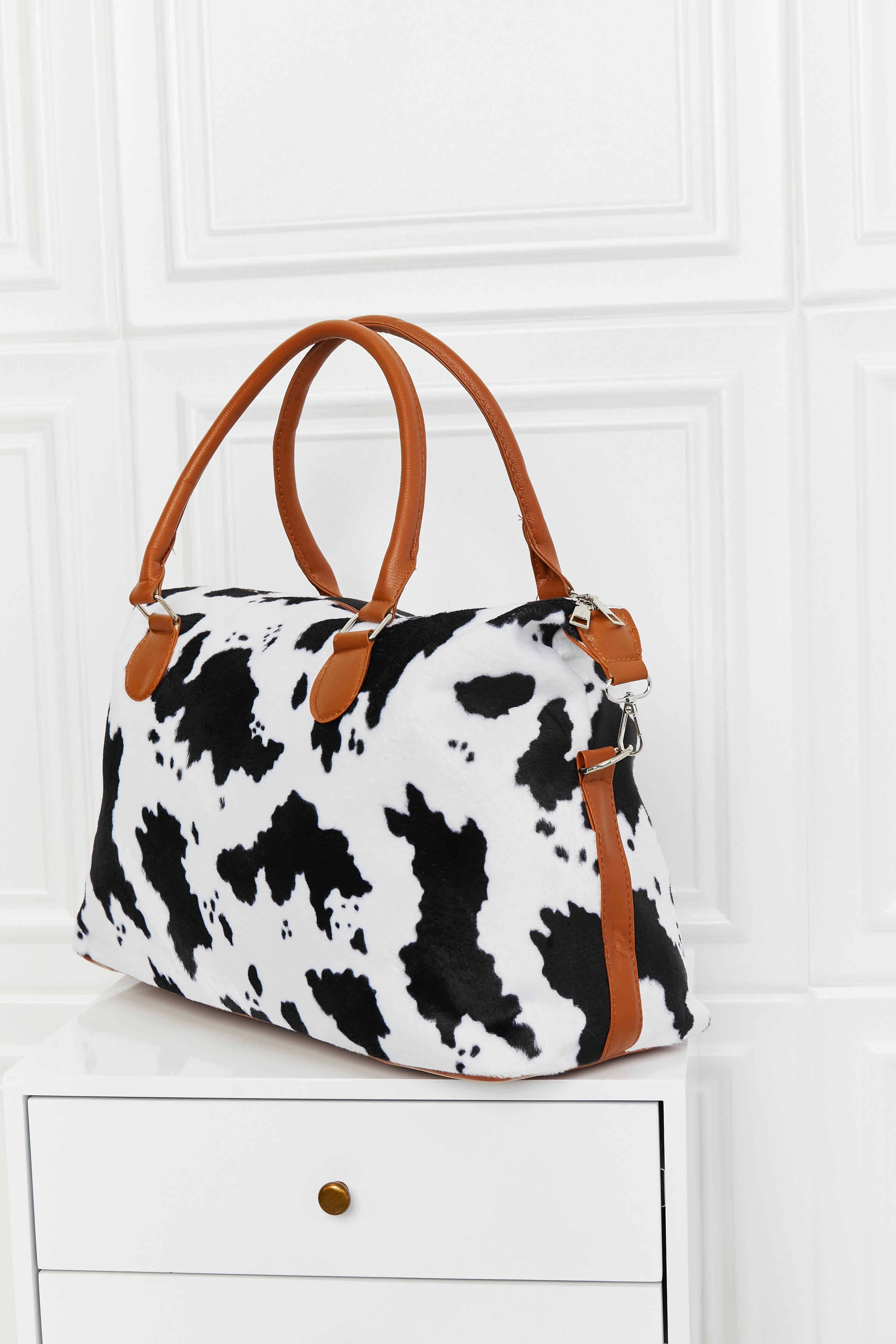 Cow print weekender bag with brown handles and zip-top opening