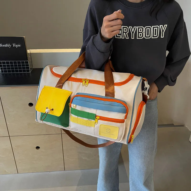 Beige duffle bag with orange edge, brown strap, and front zip pockets with colorful panels