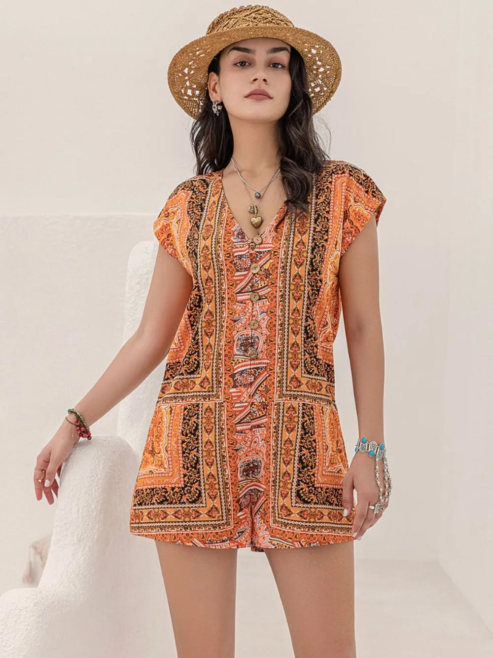 Printed V-neck cap sleeve romper in orange with ornate motif print and buttoned front
