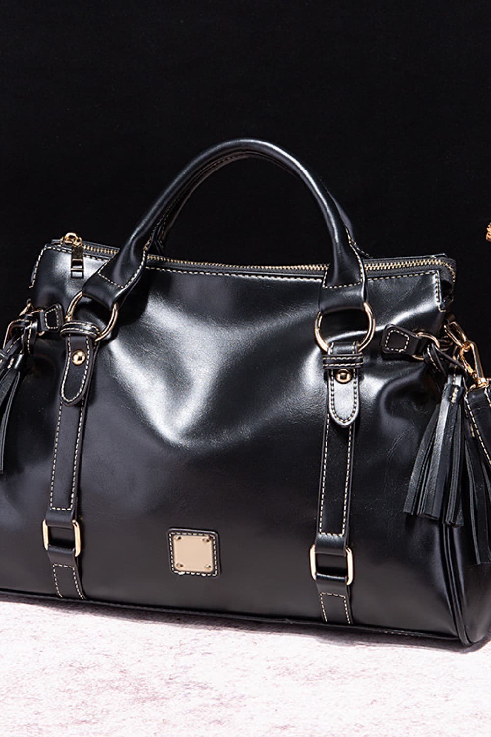 PU leather handbag in dark color with tassels, top handles, and front square patch.