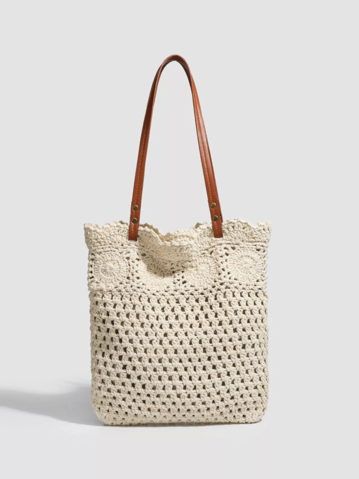 Crochet tote with rounded top and brown leather handles; cream openwork knit body.