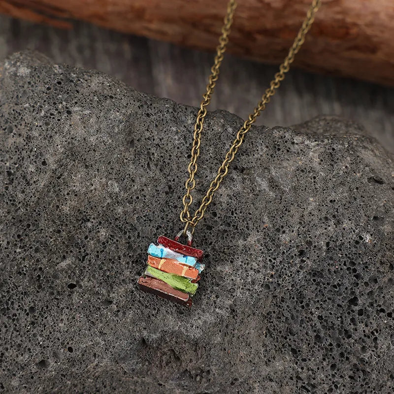 Gold-tone pendant necklace with multicolor stacked book charm on gray stone