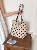 Cream polka dot shoulder bag with black dots and two black top handles on tabletop