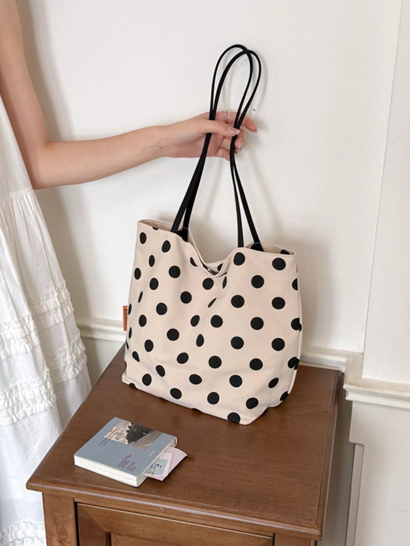 Cream polka dot shoulder bag with black dots and two black top handles on tabletop