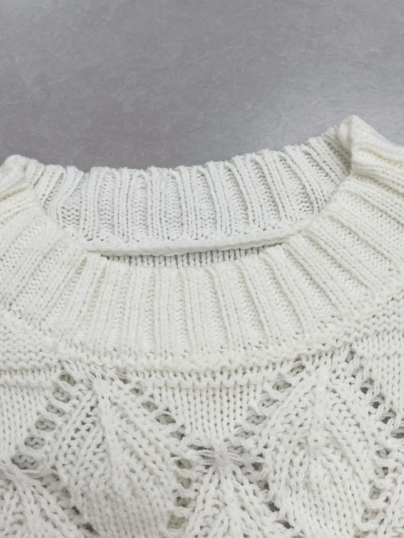 Close-up of white ribbed neckline and ruffled collar on crochet long sleeve sweater