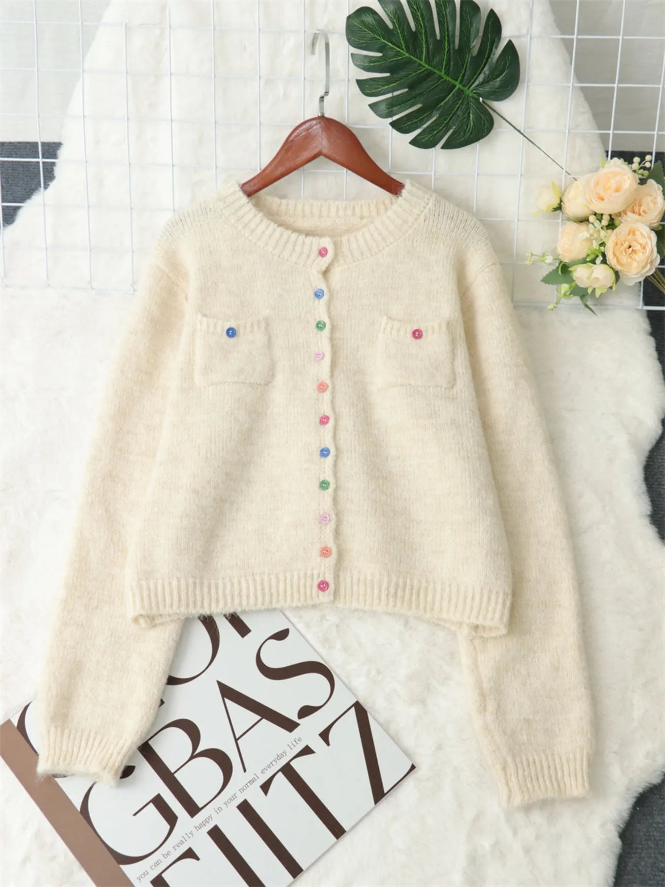 Cream cardigan sweater laid out on hanger, multicolor button front and chest pocket