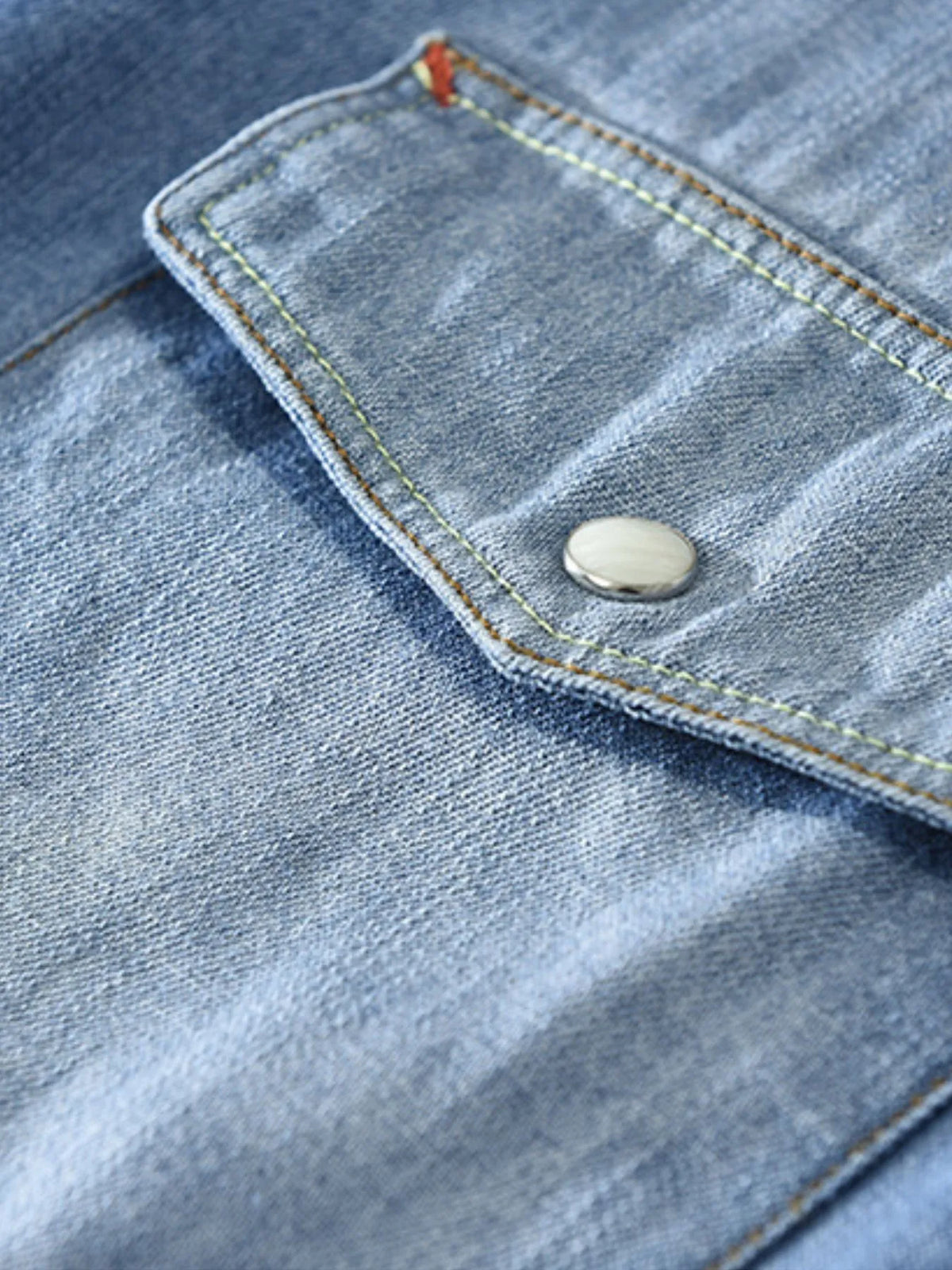 Men's denim shirt pocket flap with round button and light blue wash close-up
