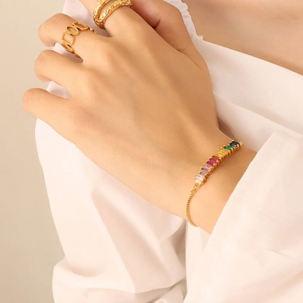 Colorful zircon tennis bracelet on wrist with gold-tone clasp details