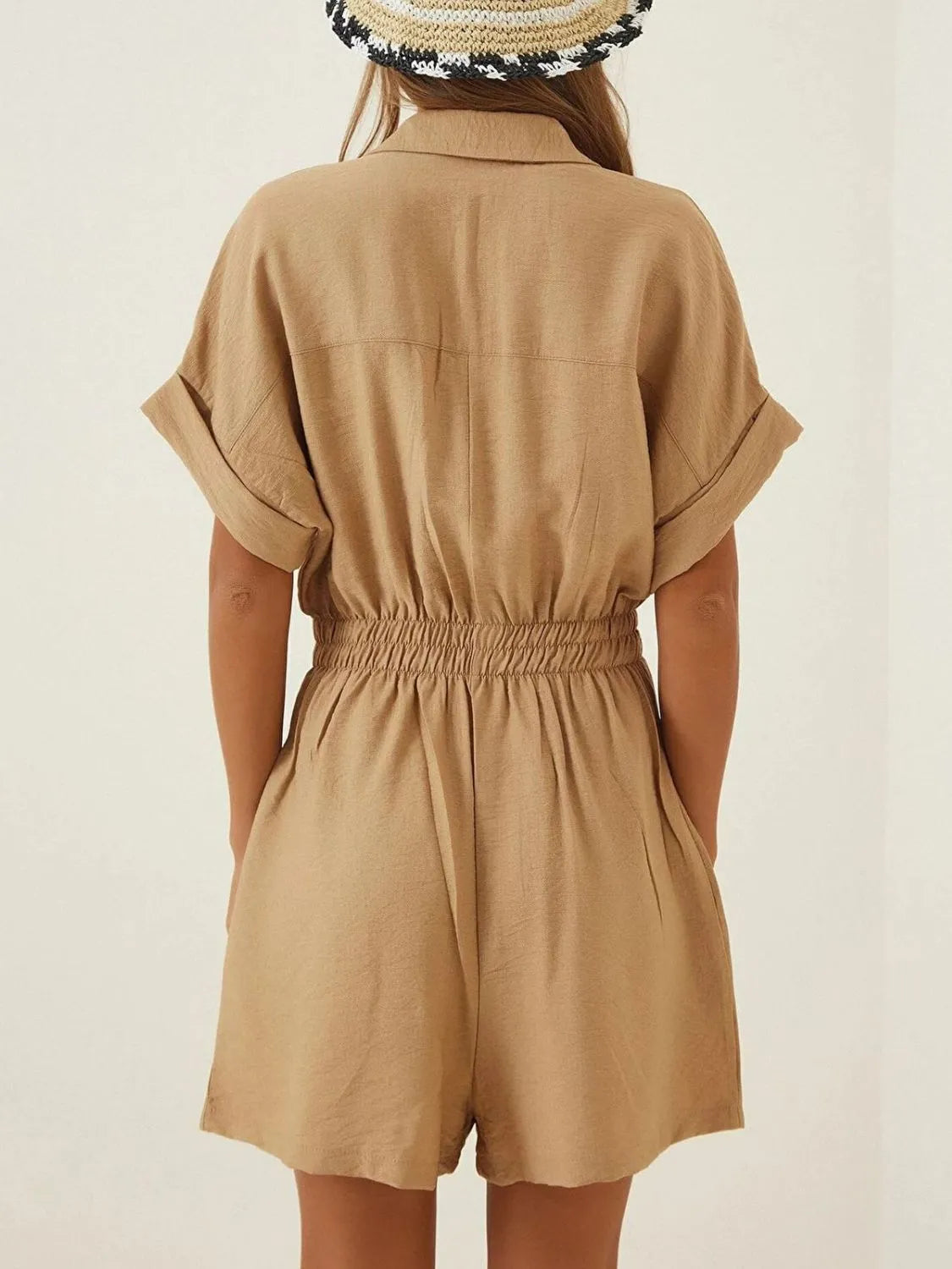 Back view of tan short-sleeve romper with collar, elastic waist, and pocketed bodice.