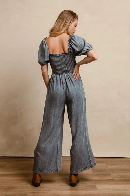 Washed denim jumpsuit from back view, smocked square back, puff sleeves, wide legs