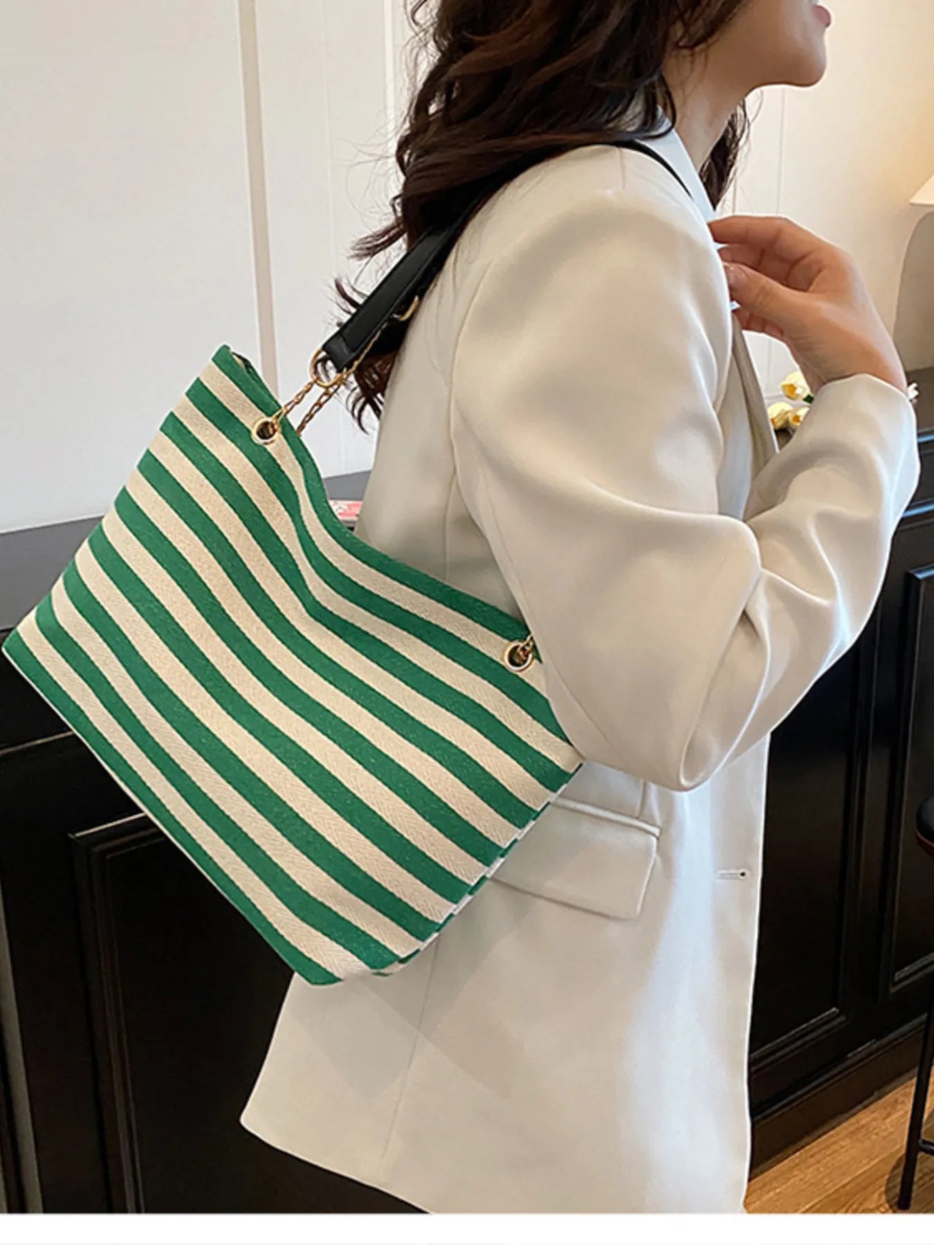 Green and white striped shoulder bag with gold chain straps, carried on the shoulder.
