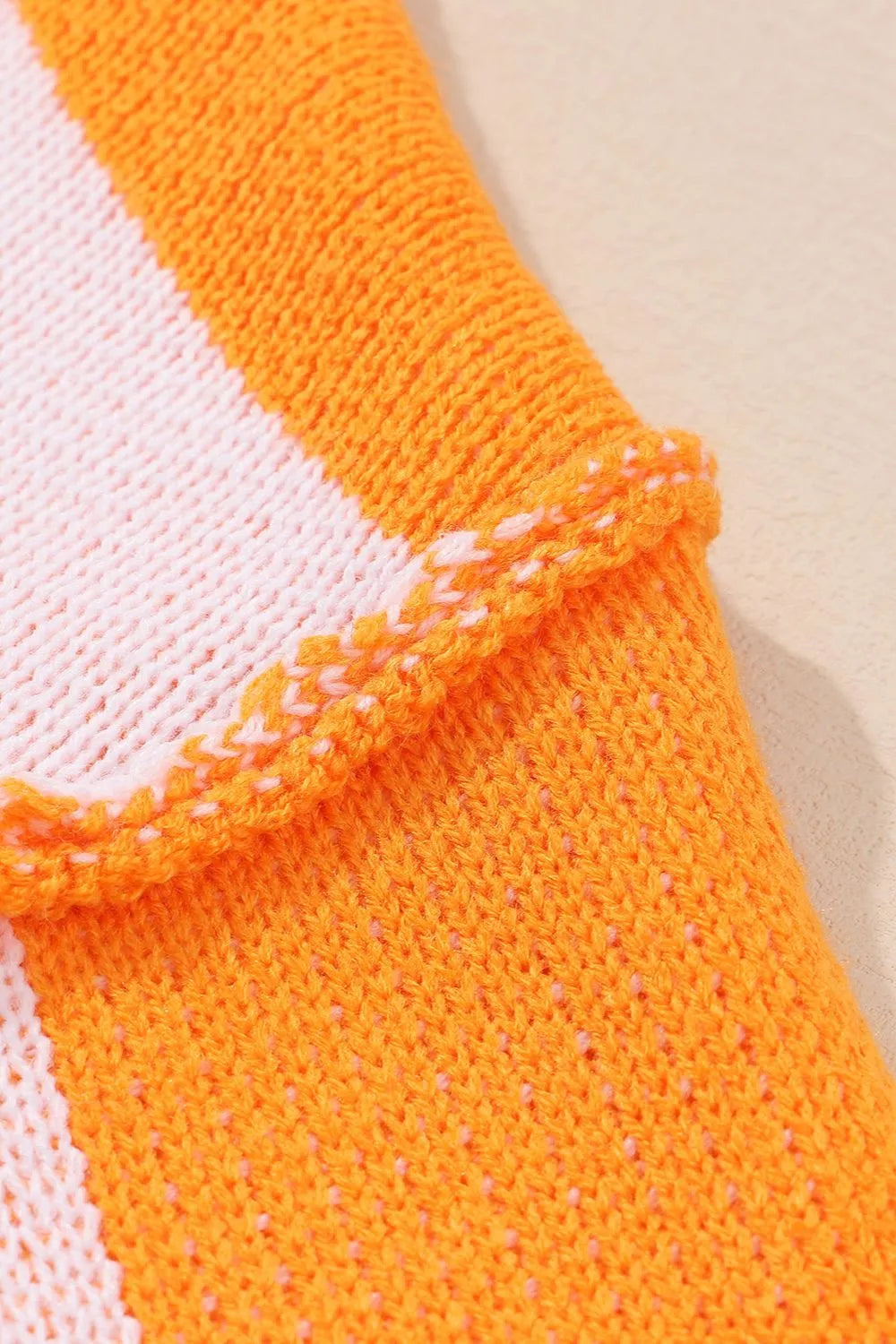 Close-up of orange knit sweater cuff with white check panel and ribbed trim