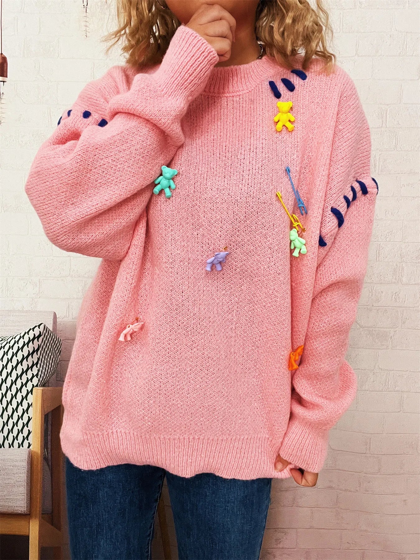 Pink round-neck knit sweater with colorful animal appliques, hand near neck, long sleeves