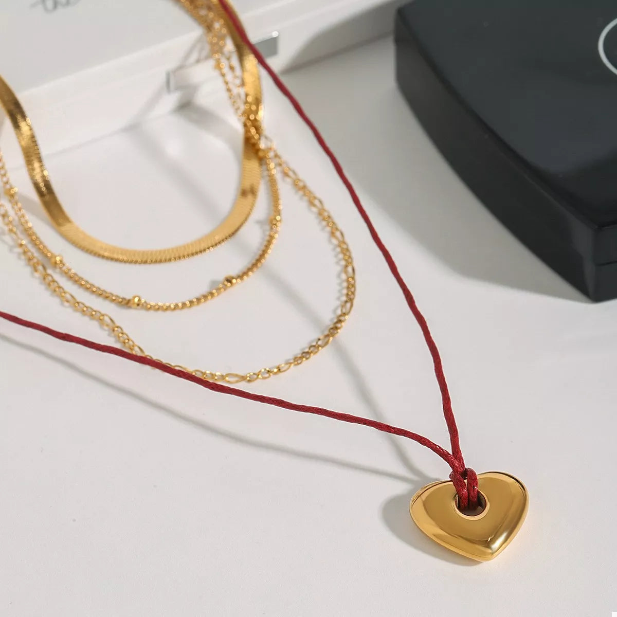 Four-layered gold heart necklace with red cord; heart charm pendant on display.