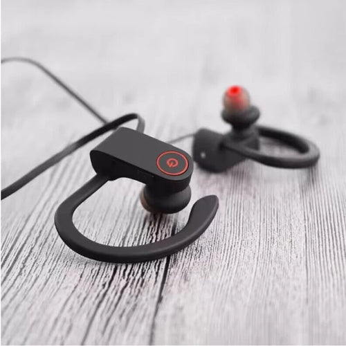 Black wireless sports ear-hook headphones resting on a tabletop with power button