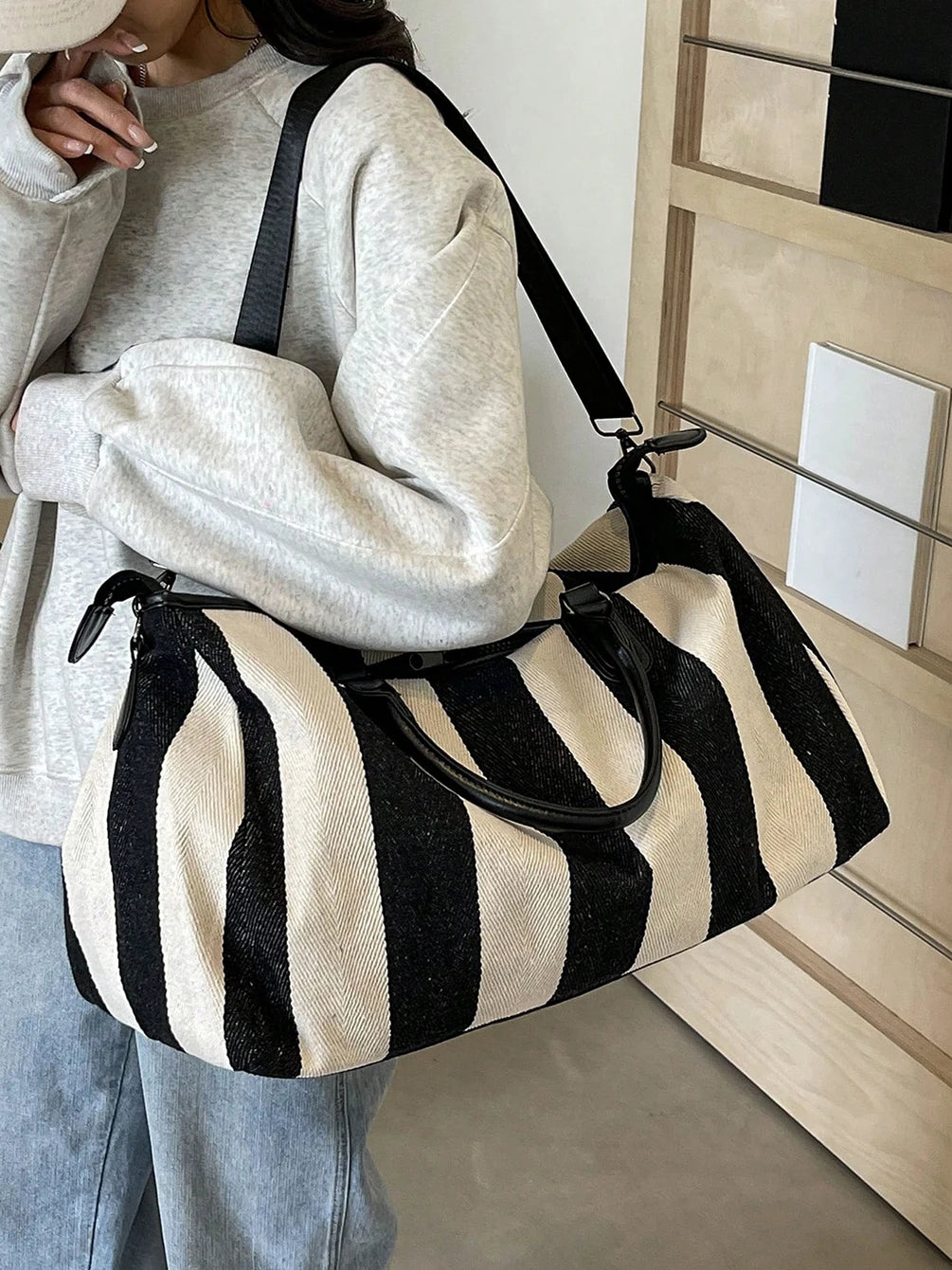 Striped weekender duffle bag worn on shoulder with crossbody strap and side zippers