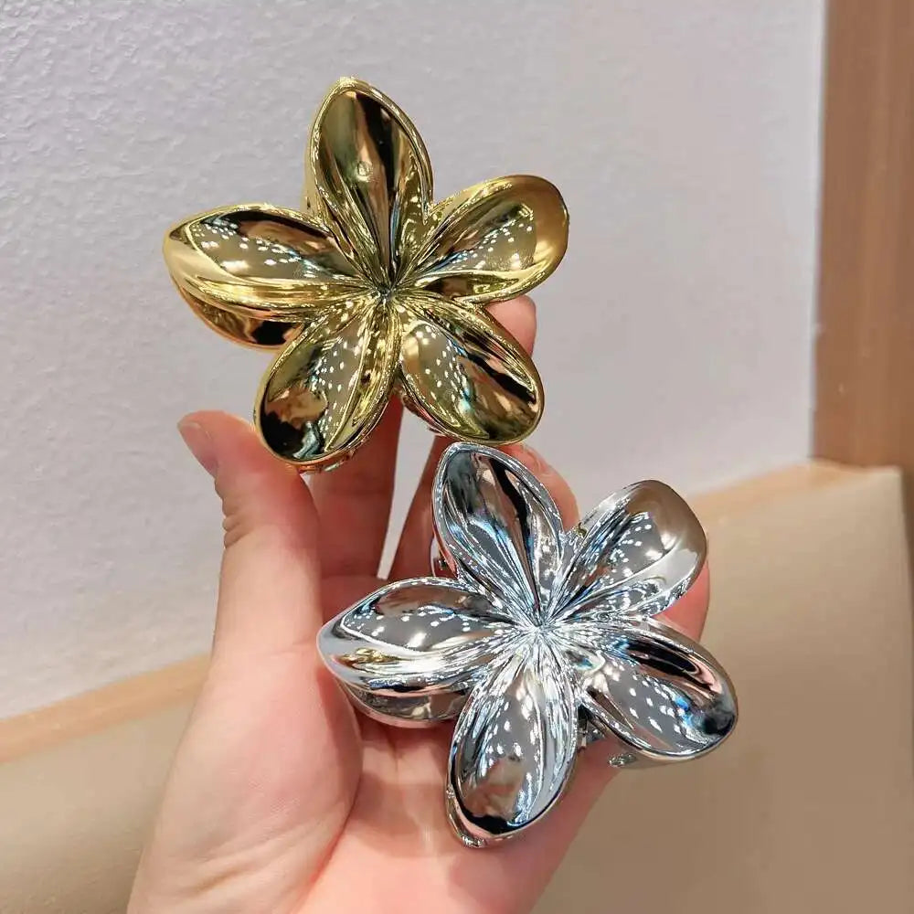 Hawaiian gradient flower hair claw clips held in hand: gold and shiny silver flower shapes