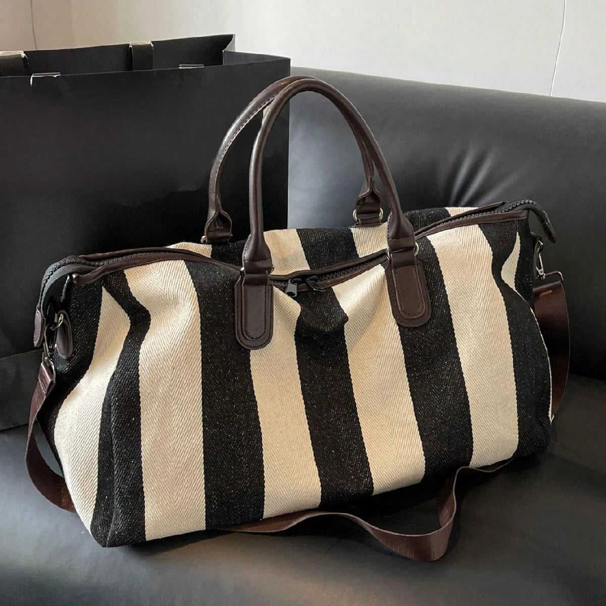 Striped duffle bag with top handles and long shoulder strap on a sofa seat