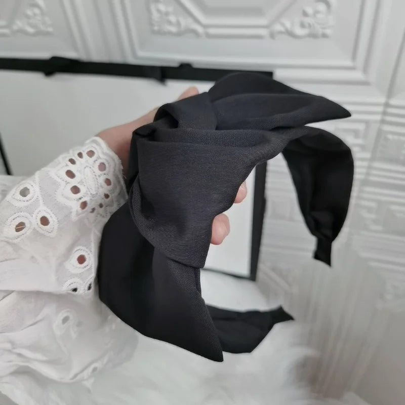 Black wide bow headband held in hand, fabric knot detail
