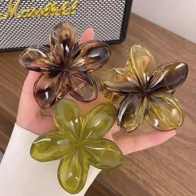 Hawaiian gradient flower hair claw clips held: olive green, gold, and translucent brown flowers