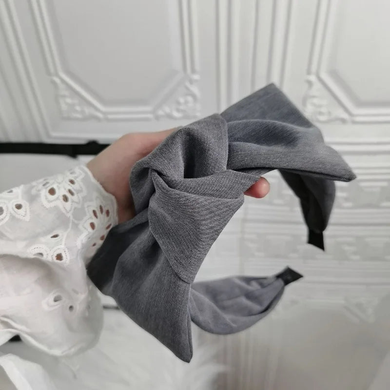 Grey wide bow headband with fabric knot, held close-up